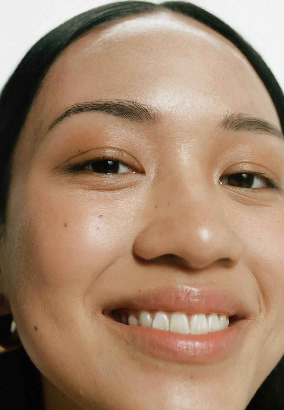 Close Up Shot of Woman Smiling Into Camera Lense. Her Skin is visibly is Soft, Smooth and Shiny