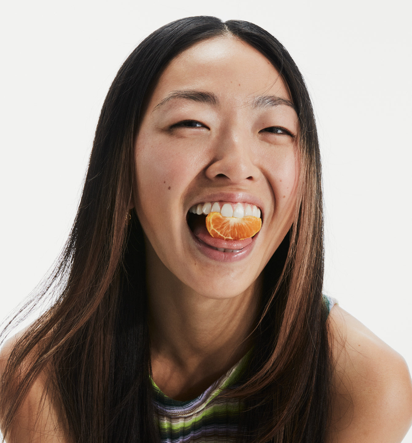 Woman with an orange segment placed in-between her teeth.